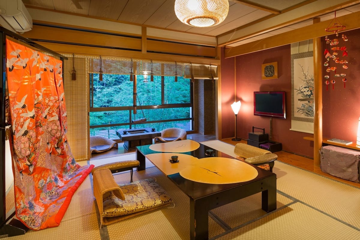 Um quarto japonês tradicional com tatames, uma mesa baixa, almofadas e uma televisão.