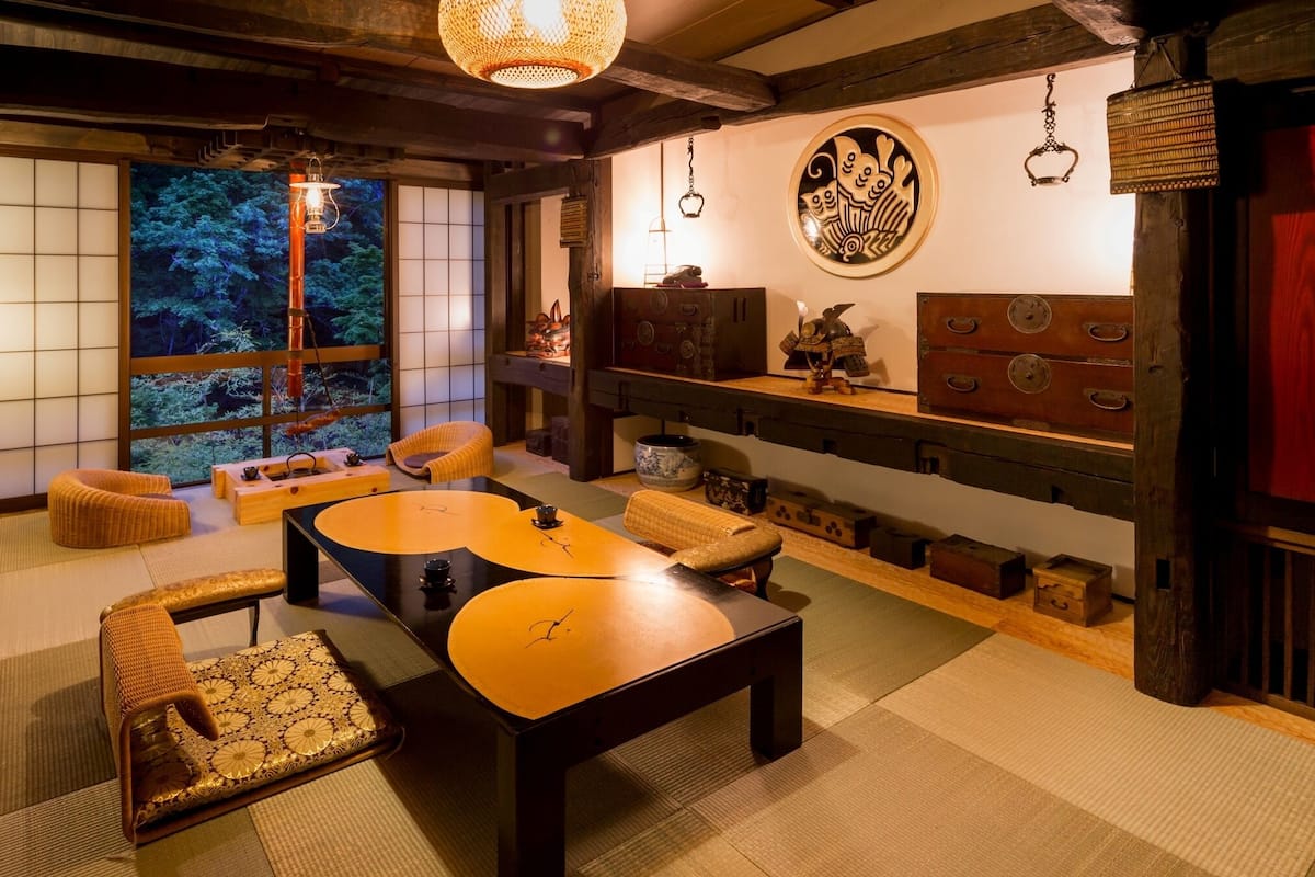 Um quarto japonês tradicional com tatames, mesinhas baixas e vista para a natureza através de biombos shoji.