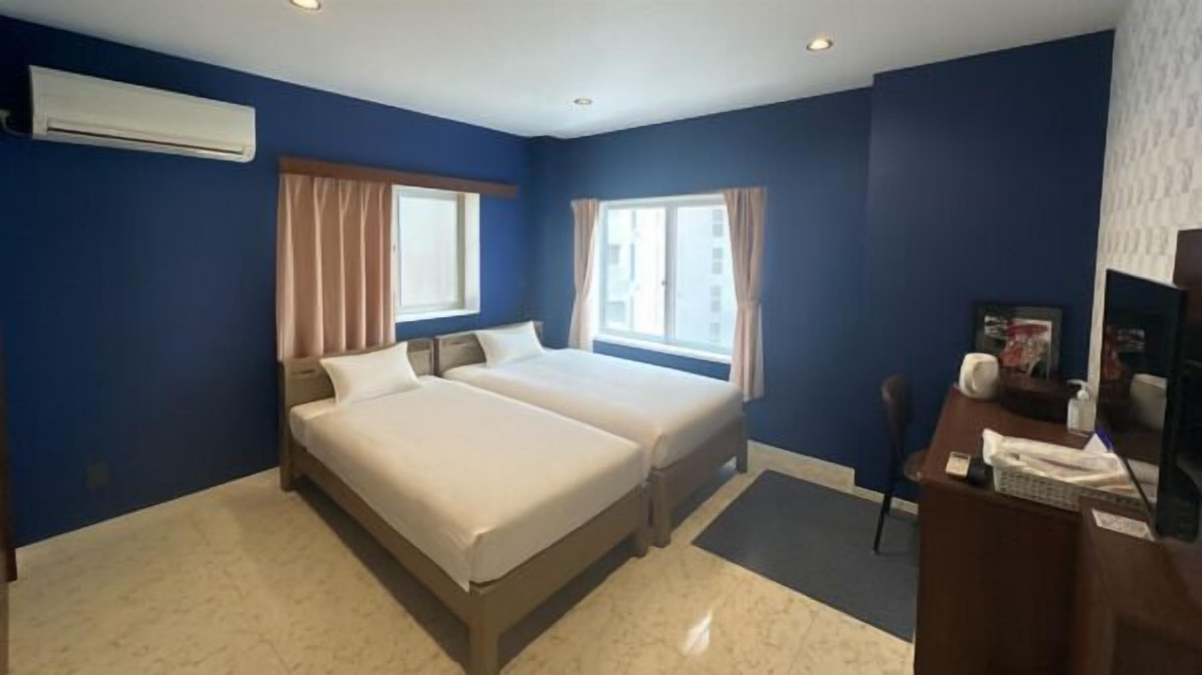 A hotel room with two beds, a desk with a chair, and a TV.
