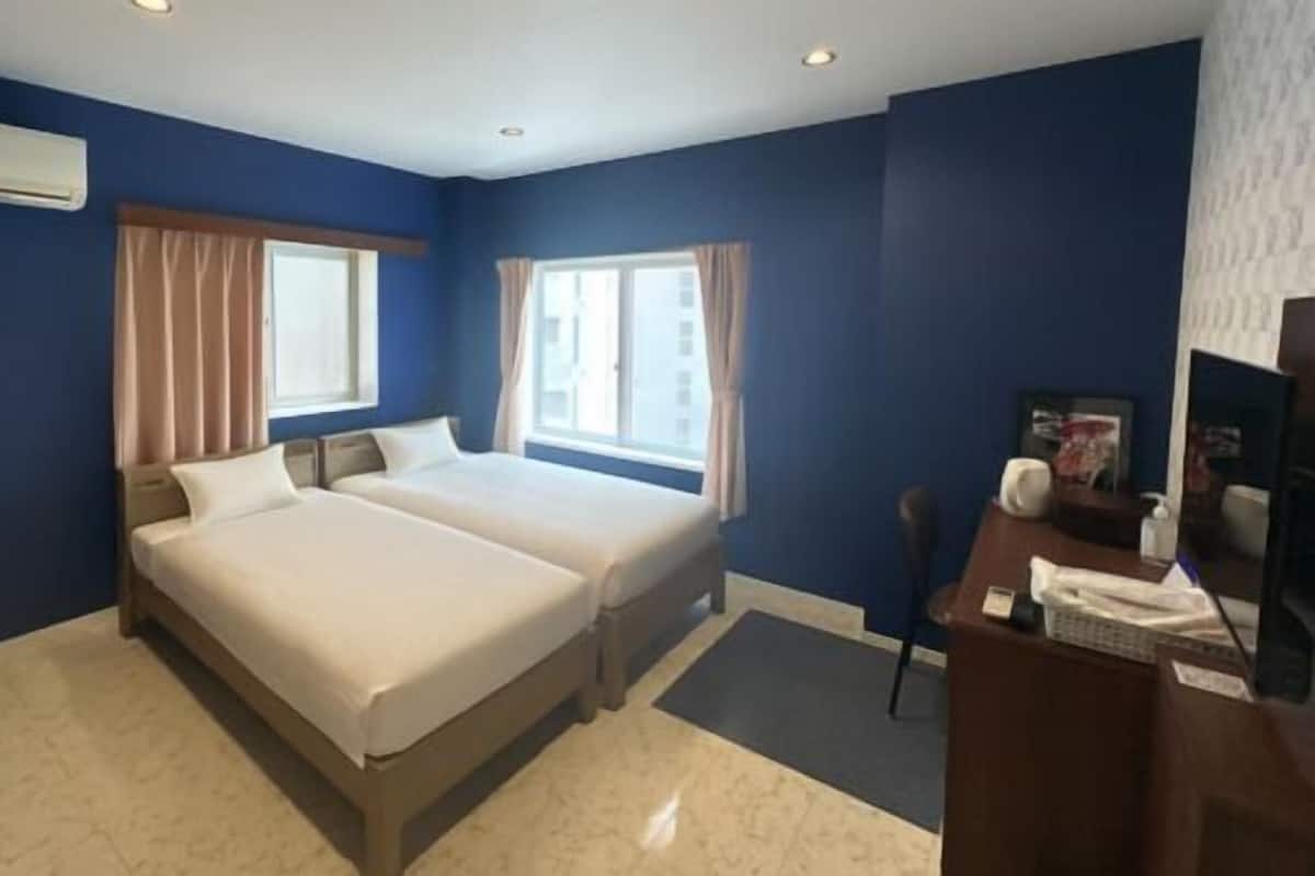 A hotel room with two beds, a desk with a chair, and a TV.