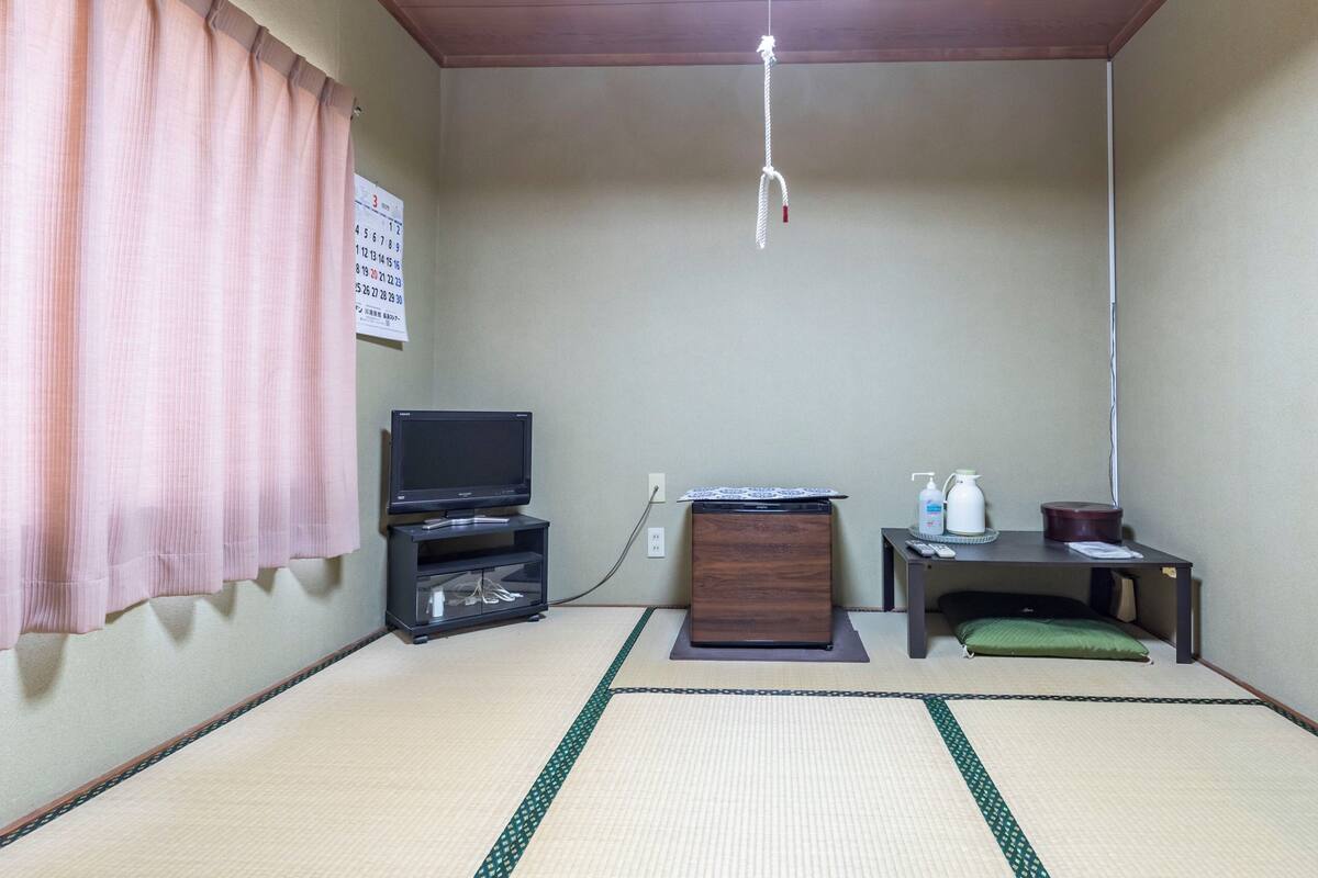A room with tatami flooring, a television, a small cabinet, a remote control, and a calendar on the wall.