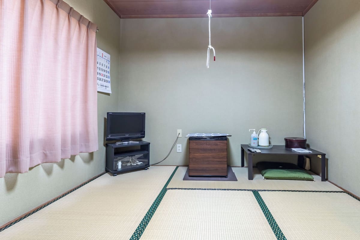 A room with tatami flooring, a television, a small cabinet, a remote control, and a calendar on the wall.
