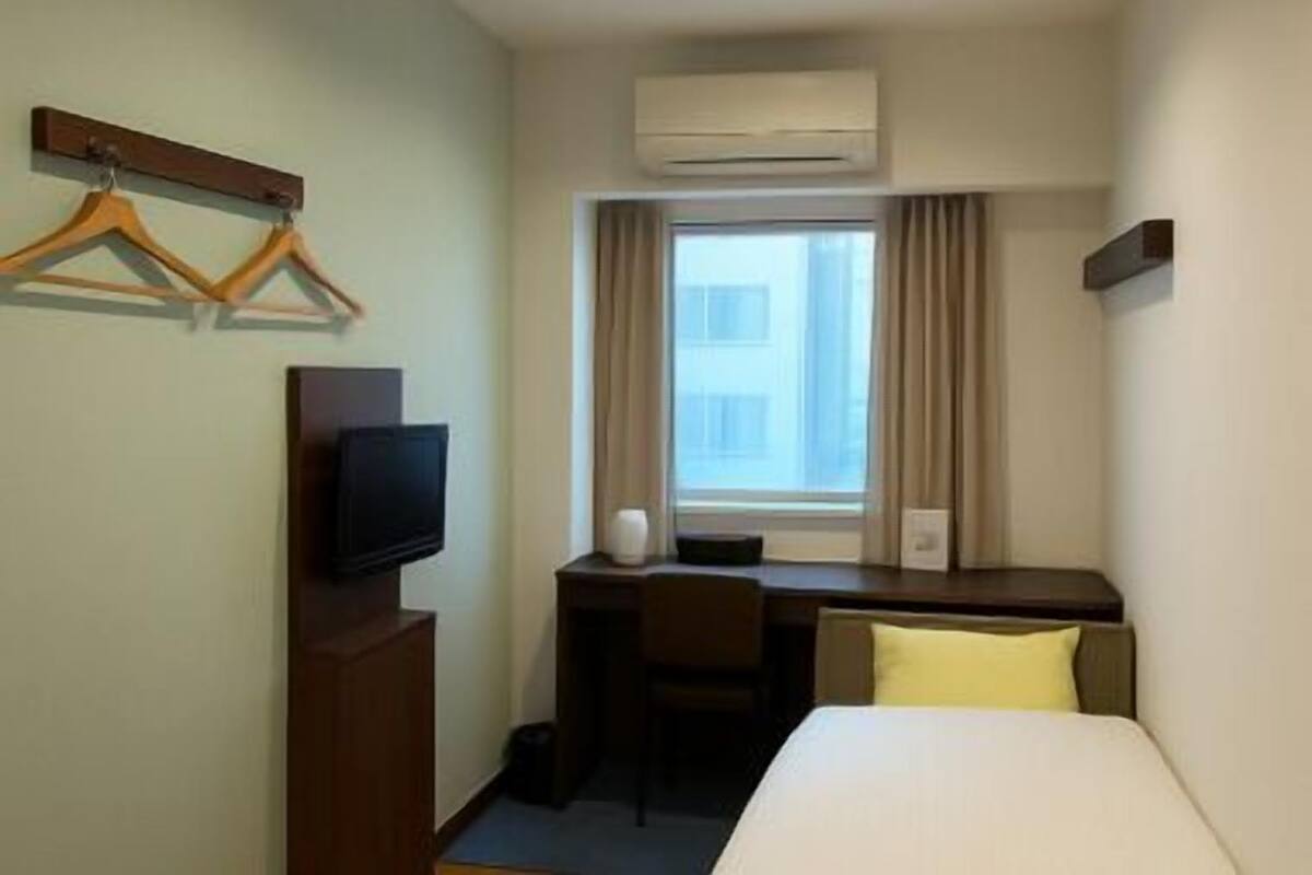 A hotel room with a bed, a desk, a television, a window with curtains, and an air conditioning unit.