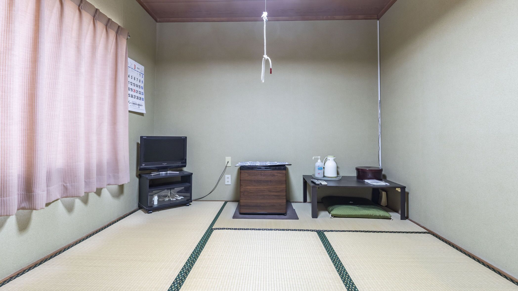 A room with tatami flooring, a television on a stand, a small table with a remote, and a cabinet.