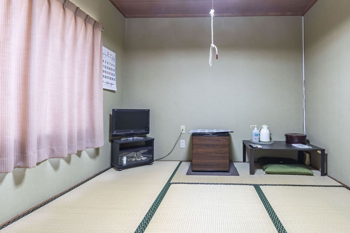 A room with tatami flooring, a television on a stand, a small table with a remote, and a cabinet.