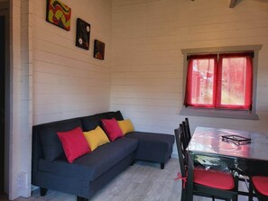 A room with a dark grey sofa with red and yellow cushions, a glass table with red chairs, and a window with red curtains.