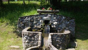 A stone well with a wooden structure on top, surrounded by grass and trees.