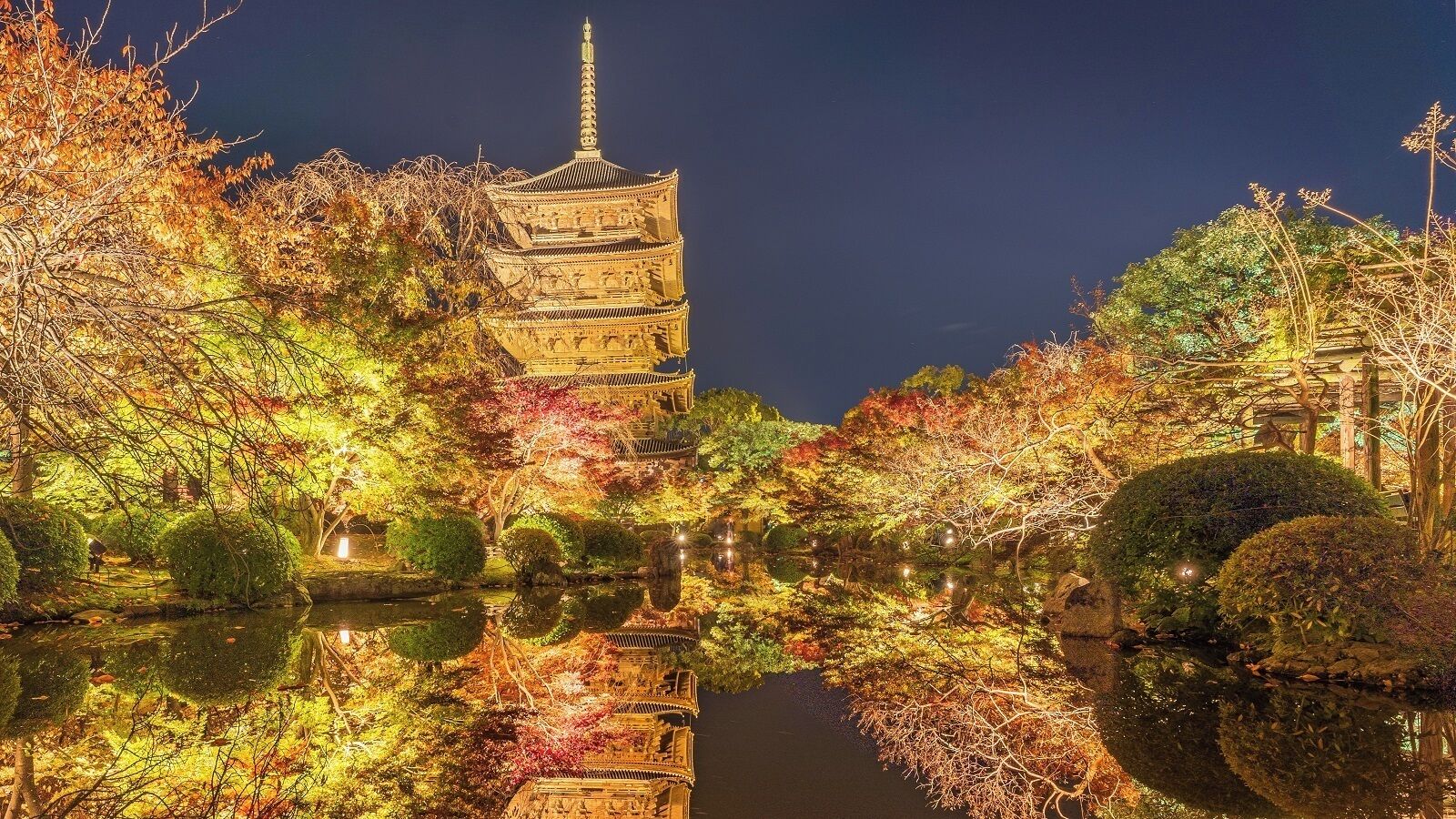 A traditional pagoda with a reflection in a calm water body, surrounded by autumn foliage.