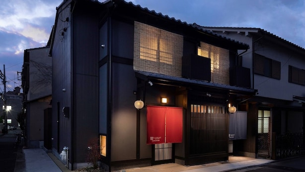 Un edificio moderno con fachada oscura, ventanas grandes y un letrero de entrada rojo.