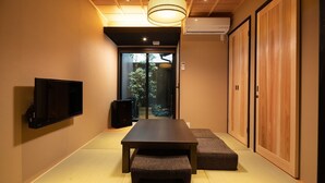 Habitación con televisión de pantalla plana en la pared, una mesa de madera con bancos, una puerta corredera que da a un jardín y un equipo de aire acondicionado instalado en el techo.