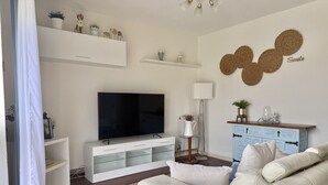 Un salon moderne doté d’un téléviseur à écran plat, de meubles blancs, d’un meuble bleu et d’œuvres d’art décoratives murales.