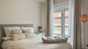 Une chambre à coucher avec un lit, une table de chevet, une fenêtre avec des rideaux et une lampe sur pied.