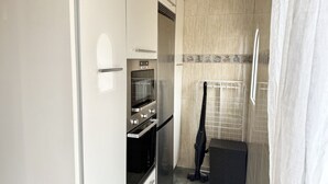 Une cuisine compacte dotée d’un four et d’un micro-ondes encastrés, d’une petite poubelle noire et d’un crédence carrelée.
