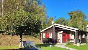 A small wooden building with a red door and a satellite dish on the roof, surrounded by a grassy area and trees. - "3 Seigneurs" Chalet de Montorgueil (Saurat)