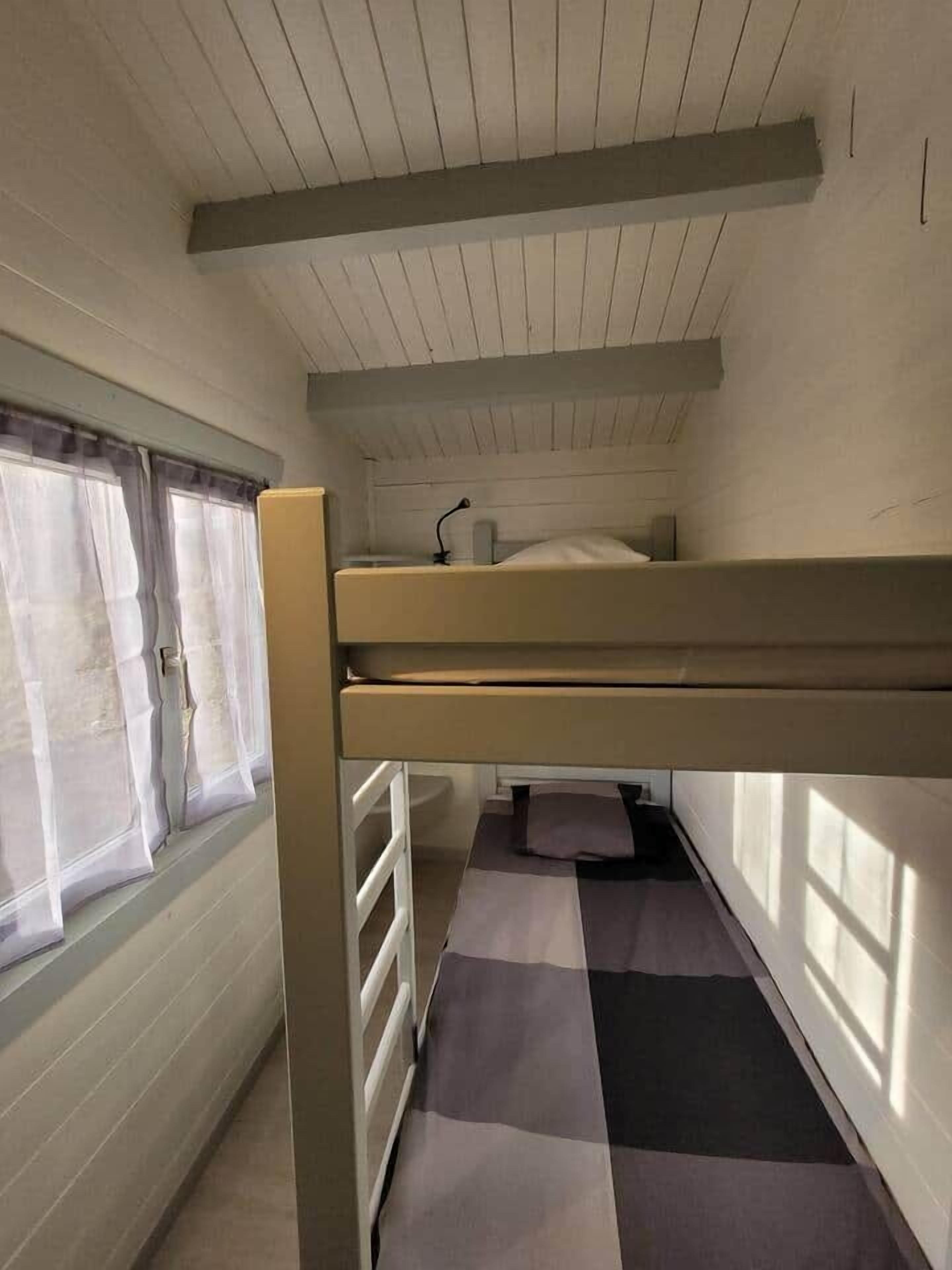Une chambre avec un lit superposé, une fenêtre, un bureau et une chaise.