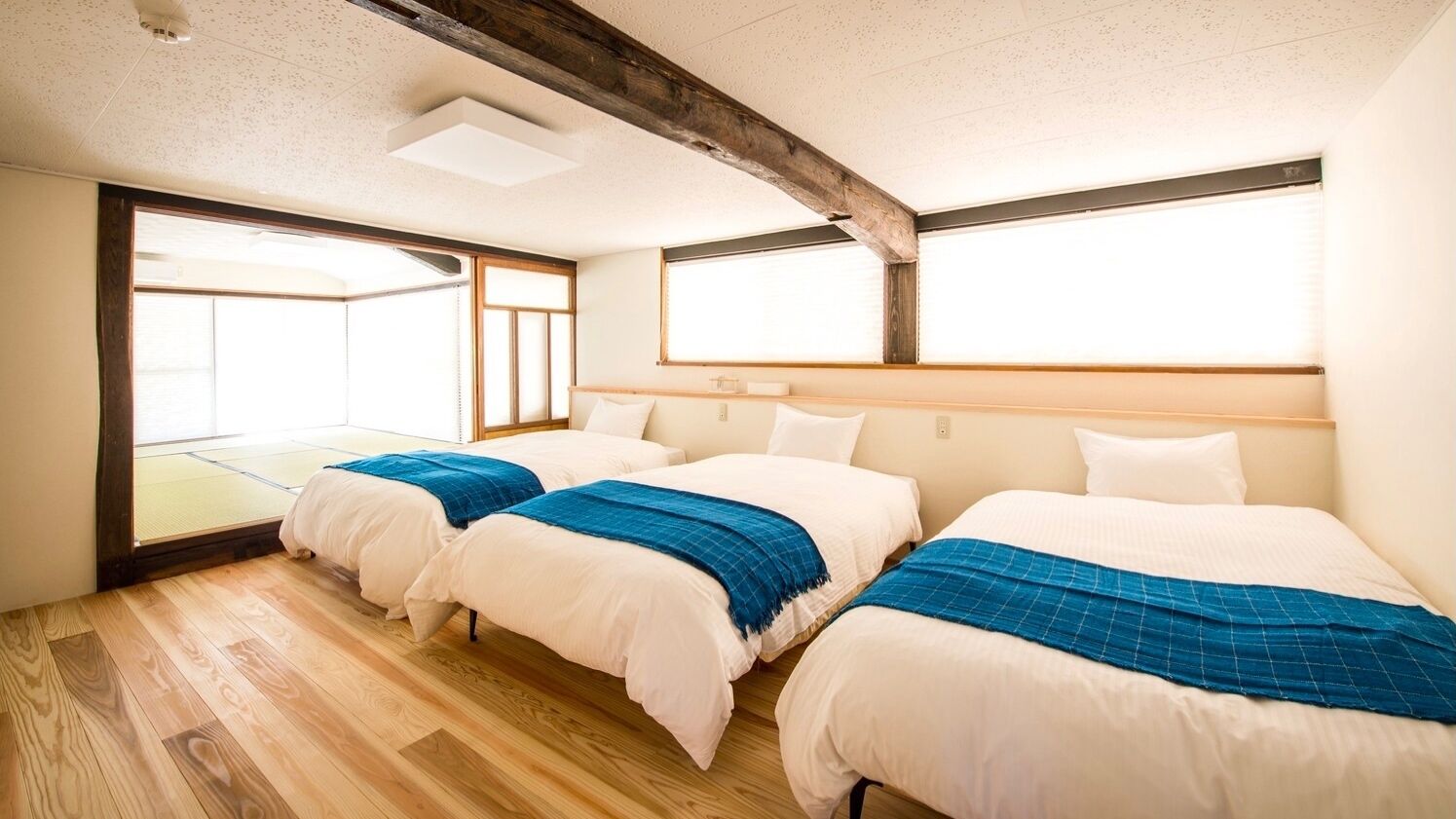 A hotel room with two beds, wooden flooring, a large window, and a view of a traditional Japanese room.