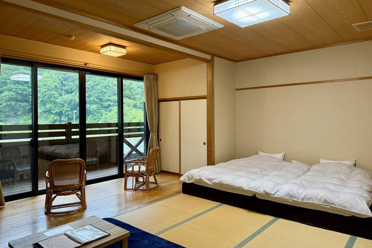Una habitación con una cama, dos sillas, una mesa y vistas a zonas verdes a través de amplios ventanales.