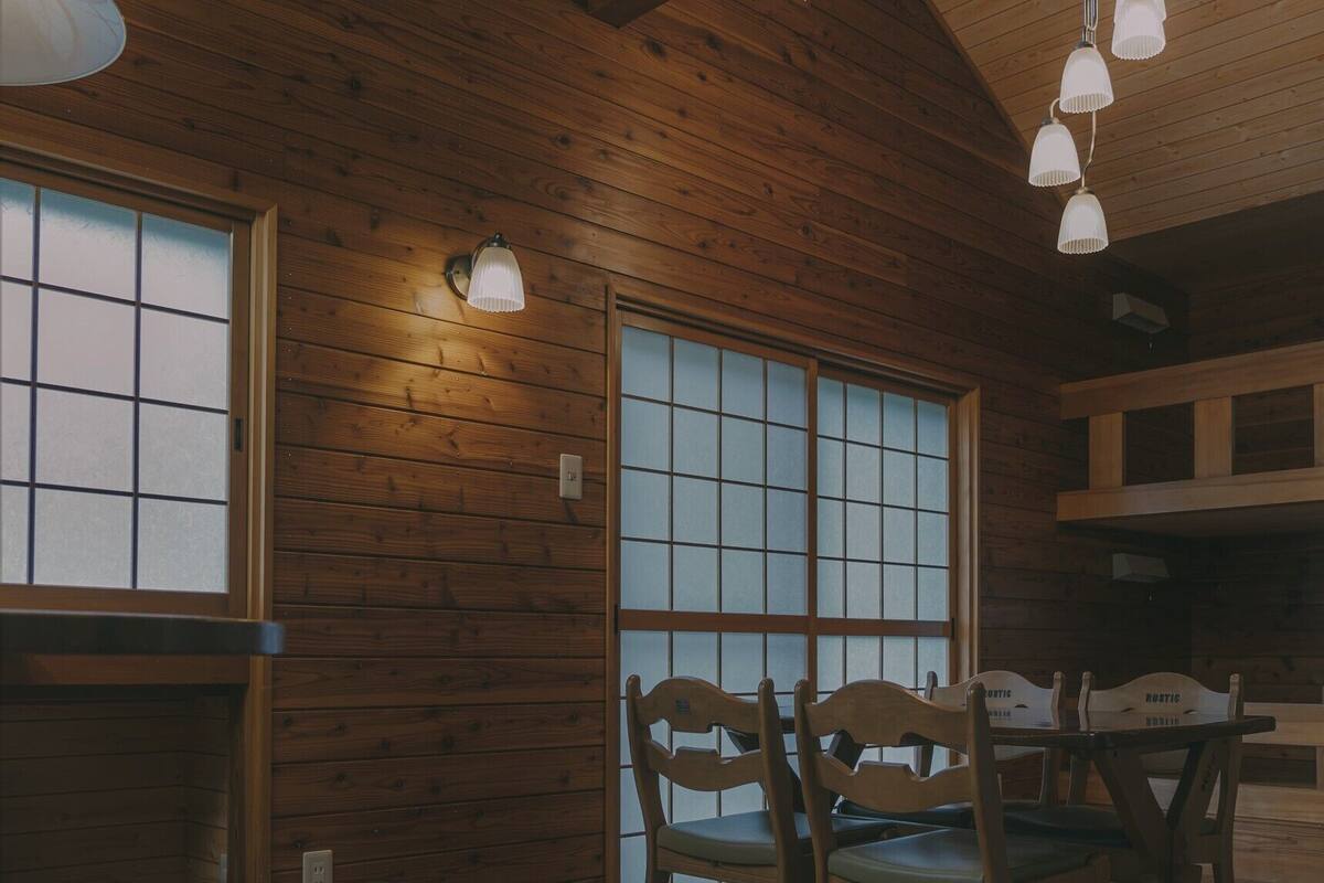 Un interior de madera con ventanas amplias, un comedor con sillas y lámparas colgantes.