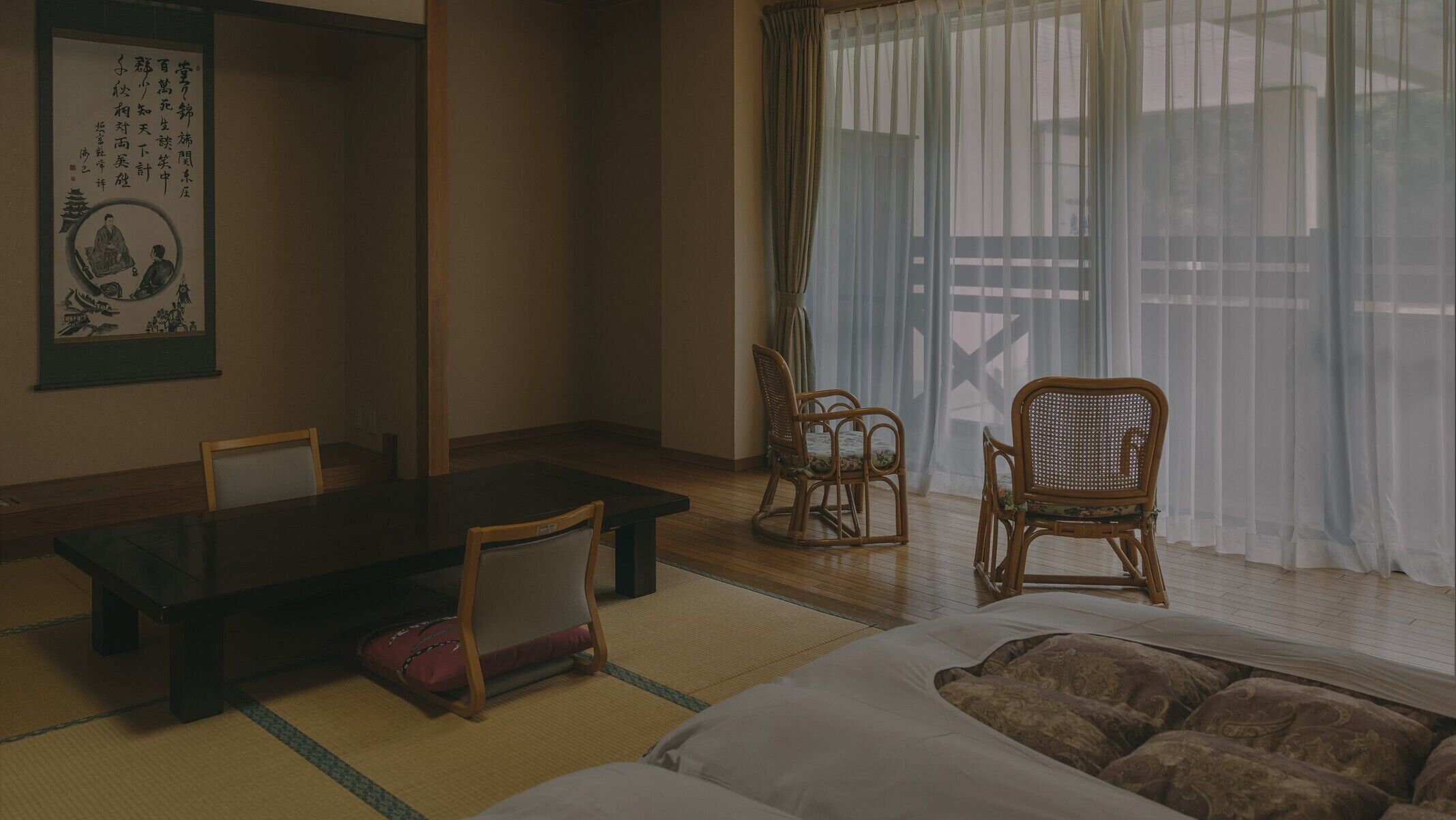 A traditional Japanese room with tatami flooring, a low table, two chairs, and a bed.