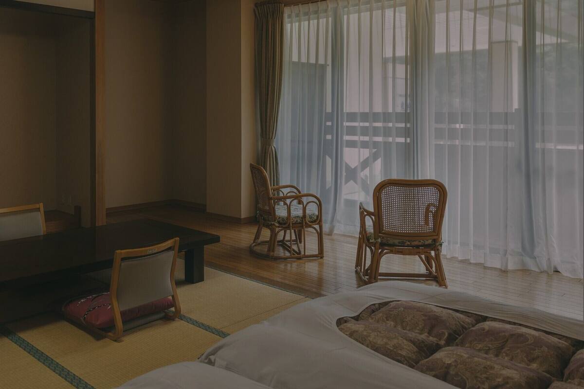 Una habitación japonesa tradicional con suelo de tatami, una mesa baja, dos sillas y una cama.