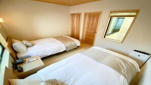 A bedroom with two beds, a desk, a laptop, and a window.