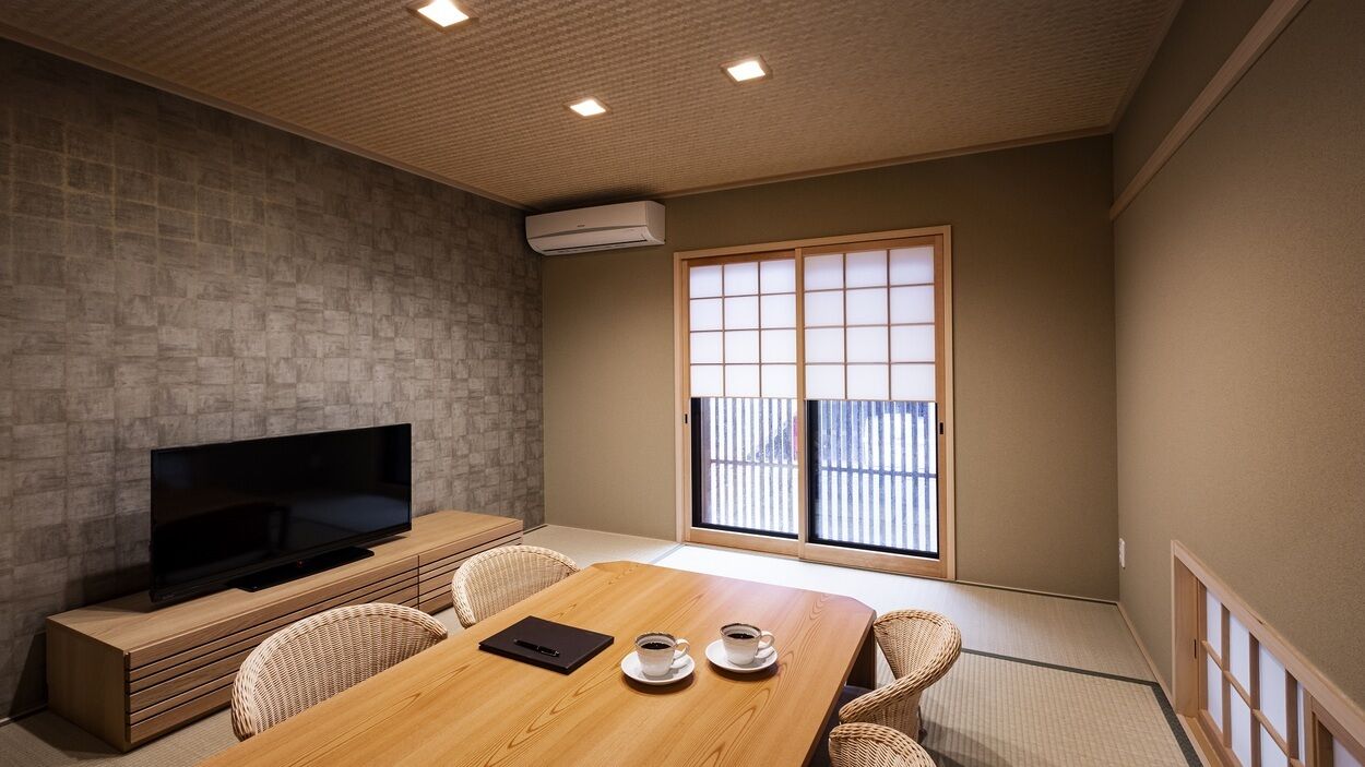 A room with a TV, a wooden table with chairs, a sliding door, and a view through the door.