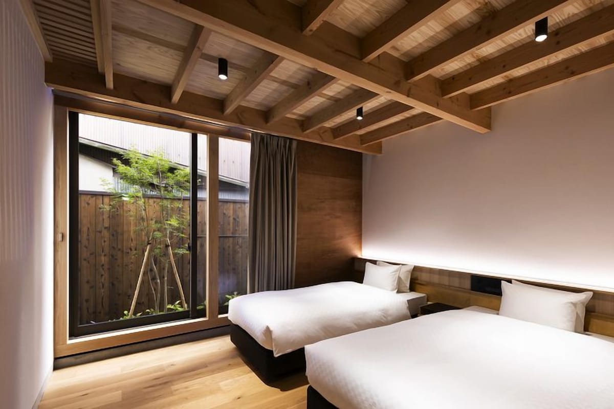 A hotel room with two beds, a large window, and a wooden ceiling.