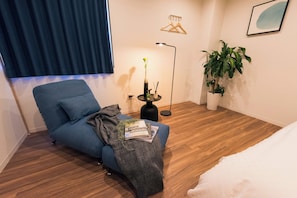A modern room with a blue sofa, a small side table with a lamp, a potted plant, and a bed. - Tora Hotel Skytree (Tokyo)