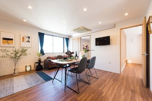 A modern living room with a dining area, wooden flooring, a sofa set, a coffee table, and a TV mounted on the wall. - Tora Hotel Skytree (Tokyo)