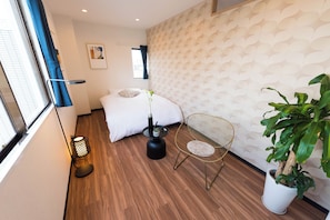 A modern hotel room with a bed, a small side table, a chair, a potted plant, and a decorative wall. - Tora Hotel Skytree (Tokyo)