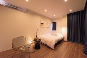 A modern bedroom with a bed, a chair, a small table with a hat, and a vase with flowers. - Tora Hotel Skytree (Tokyo)