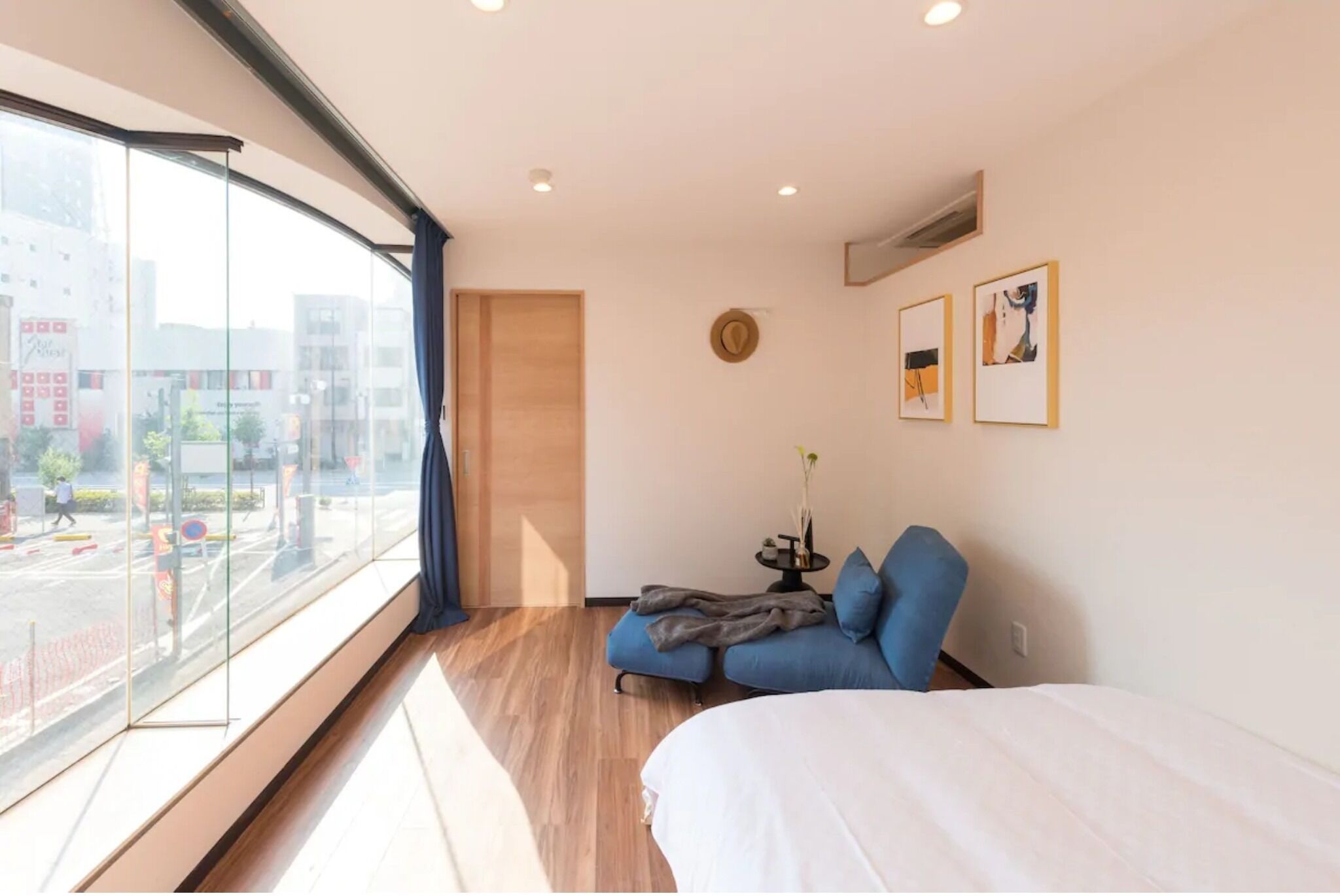 A modern hotel room with a large window, a bed, a sofa, and a small table with a vase.