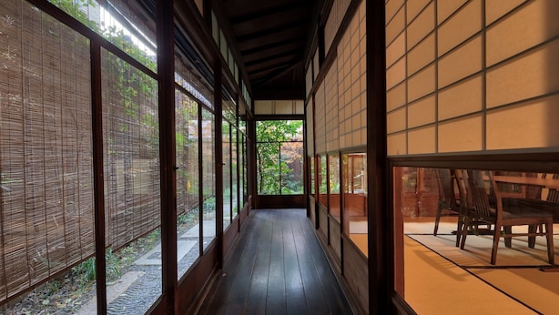 Ett traditionellt japanskt rum med tatamimattor på golvet, skjutdörrar och utsikt över en trädgård.