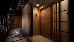 En traditionell japansk entré med en trädörr, en gång av sten och en väggmonterad lampa.
