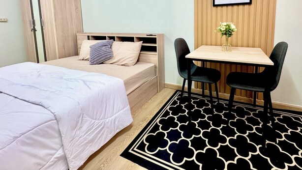 Un dormitorio con una cama, una mesita de noche y un escritorio con dos sillas. Hay una cita enmarcada en la pared y una alfombra estampada en el suelo.