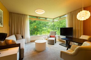 A modern living room with a sofa, ottoman, round coffee table, and a TV. - The Green Leaf Niseko Village, Tapestry Collection (Niseko)