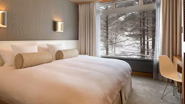 Una habitación de hotel con una cama grande, una ventana que da a árboles y una silla.
