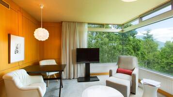 A modern hotel room with a large window, a flat-screen TV, a dining table, and two chairs.