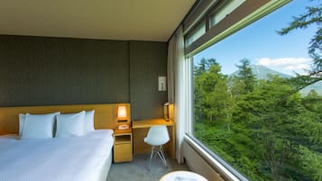 Habitación de hotel con cama, escritorio, silla y vistas a un bosque y una montaña.