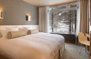Una habitación de hotel con una cama grande, una ventana que da a árboles y una silla.