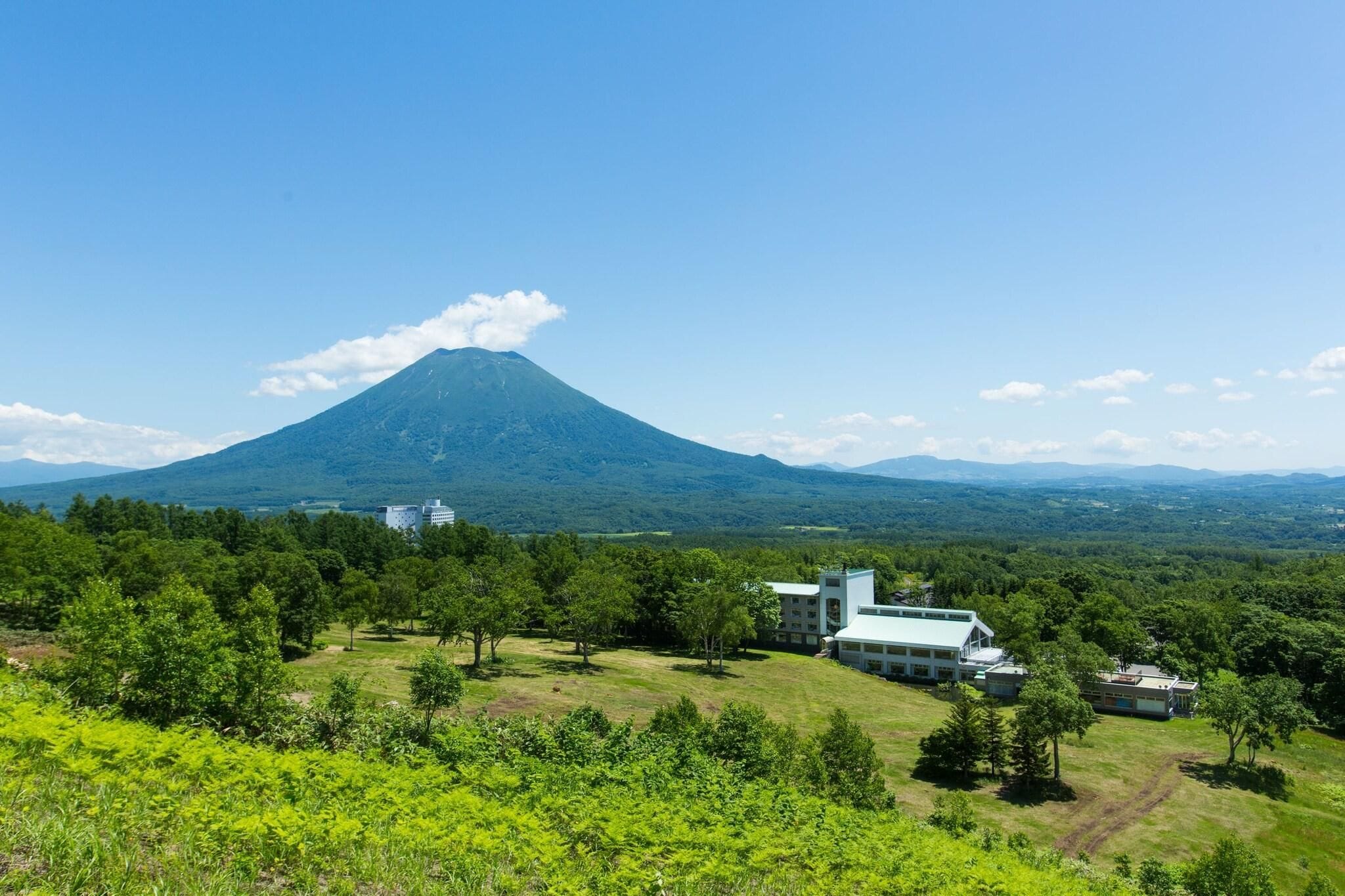 A mountain with a small building in the foreground and a larger building in the background.