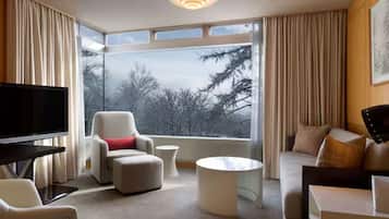 Una habitación de hotel moderna con un ventanal grande, un televisor de pantalla plana, un sofá, una silla y una mesa de centro.