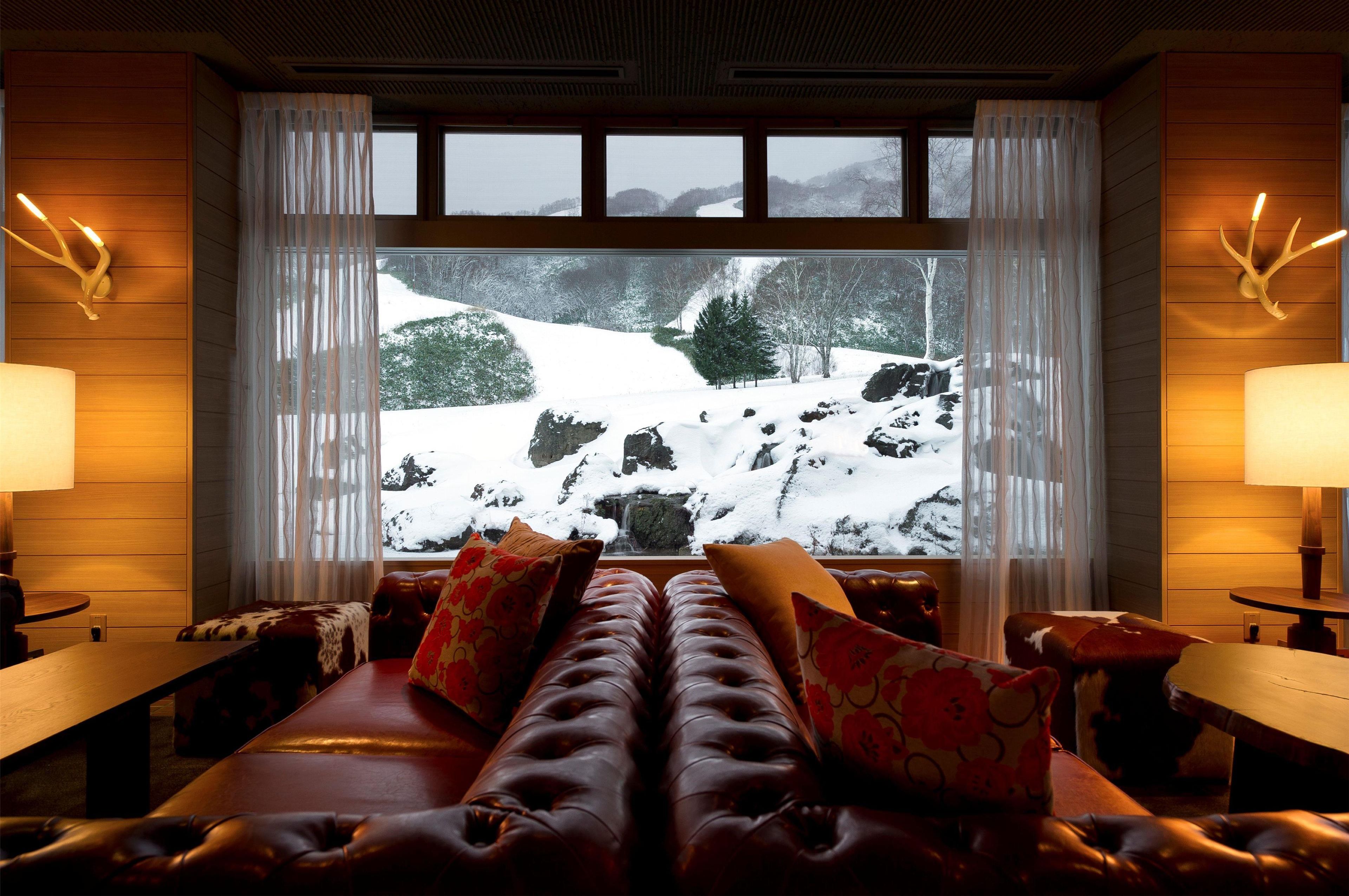 Una habitación acogedora con un sofá de cuero, una mesa de madera y un ventanal con vistas nevadas.