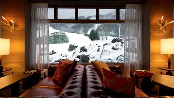 Una habitación acogedora con un sofá de cuero, una mesa de madera y un ventanal con vistas nevadas.