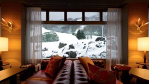 Una habitación acogedora con un sofá de cuero, una mesa de madera y un ventanal con vistas nevadas.