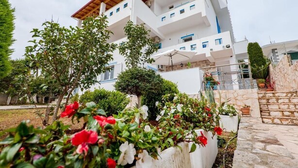 Um edifício com várias andares e varandas, rodeado por vegetação e plantas em vasos.