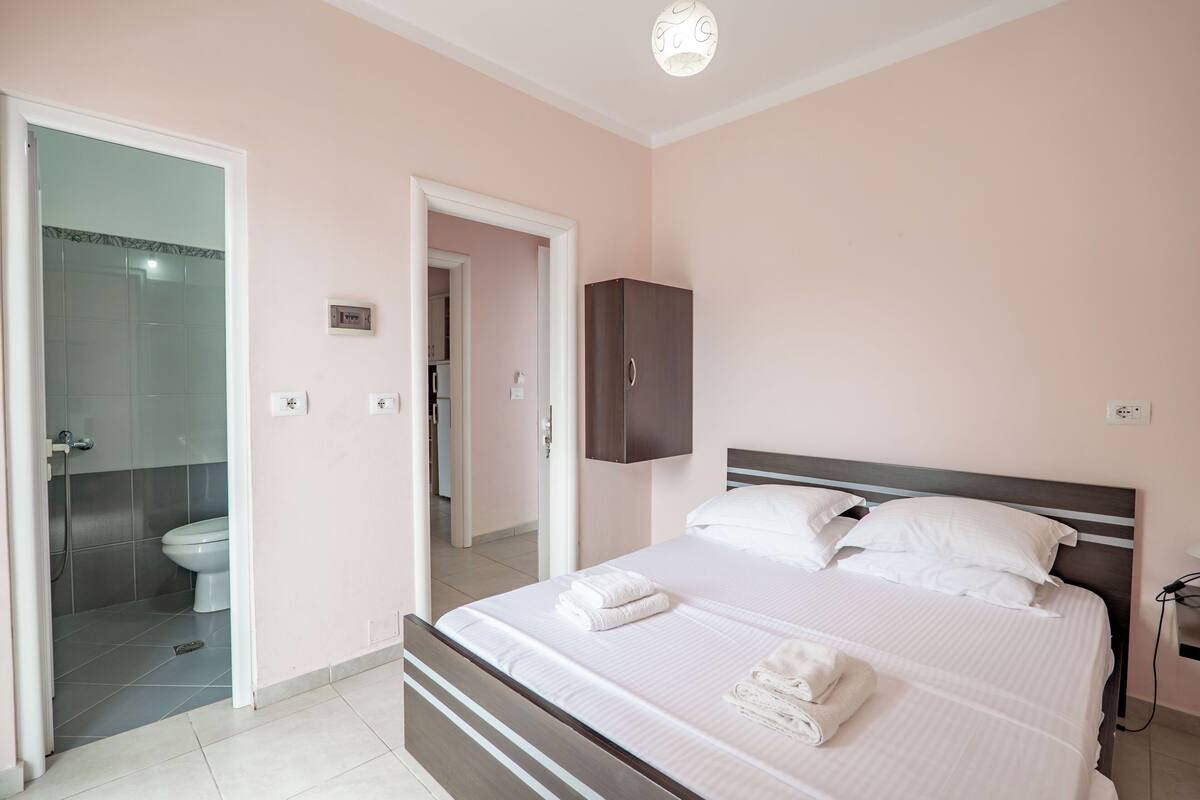 A bedroom with a bed, a wardrobe, a bathroom with a toilet, and a shower.