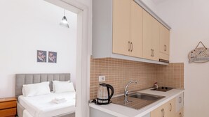 Quarto com cama, mesa de cabeceira e um pequeno criado-mudo. Ao lado do quarto, há uma cozinha compacta com pia, fogão e chaleira.