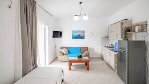 Um espaço de estar compacto com cama, sofá, mesa de centro, TV, cozinha e geladeira.