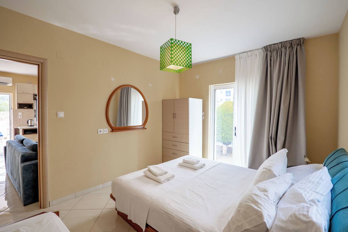 A hotel room with a bed, a wardrobe, a mirror, and a view of the outside.